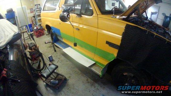 Yellow Ford Bronco with green and blue stripes on the side, hood open, in a garage with tools around