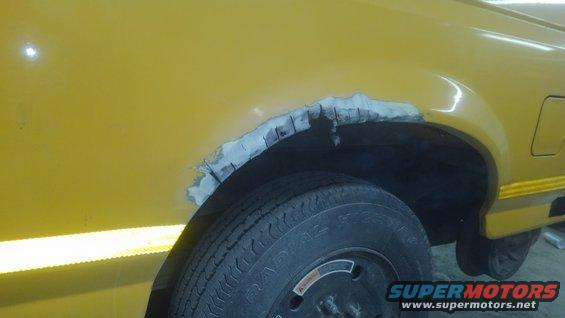 yellow vehicle's rear wheel well shows rust damage and body filler