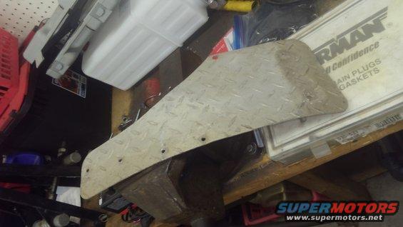 Diamond plate metal piece with mounting holes, resting on a workbench with parts and packaging