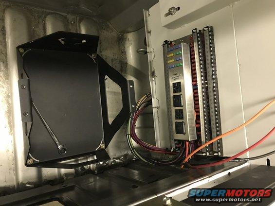 Vehicle interior showing a fuse box with colorful fuses and wiring, plus a black bracket with a wrench on it