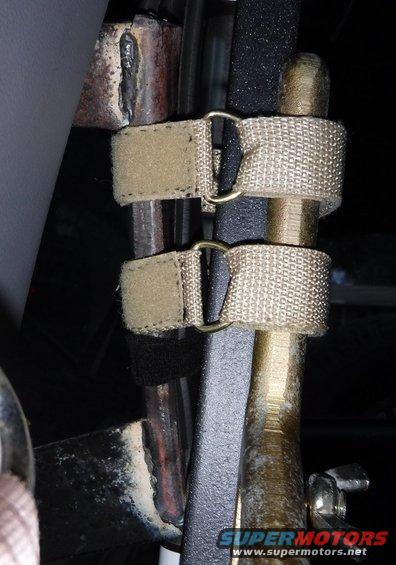 Straps securing a Hi-Lift jack to a metal bar, showing welded metal and textured surfaces