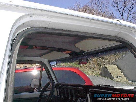 View inside a pickup truck cab, looking out the windshield. Another red vehicle is visible outside