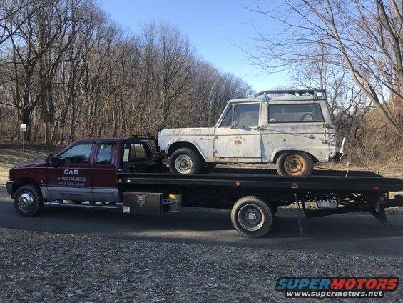 Tow truck carrying a white first-gen Ford Bronco