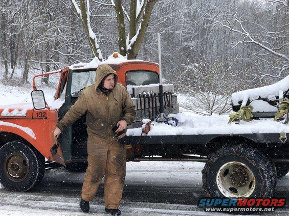 Orange truck with a man in work clothes standing in the snow, number 102 on door