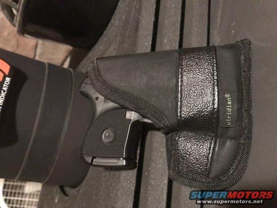 Black handgun in a black holster with "viridian" label, next to a black cylindrical object with orange text