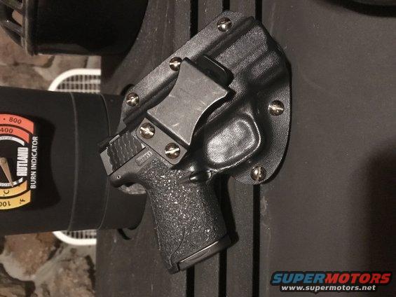 Black handgun in a black Kydex holster attached to a dark surface