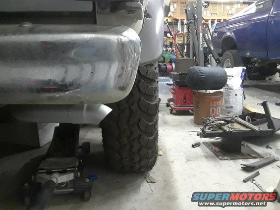 1985 Ford Bronco rear axle and tire on jack stands, blue Ford truck in background