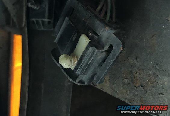 Close-up of a black electrical connector with a white plastic piece and wires. A yellow light is visible on the left