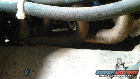Close-up of exhaust manifold pipes and a heater hose with text