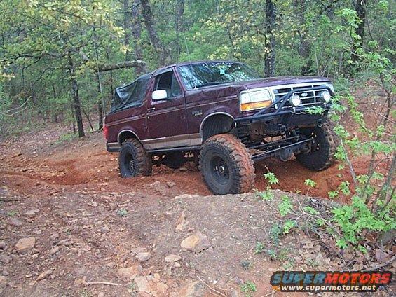 Maroon Ford Bronco with off-road tires and bumper driving on a dirt trail