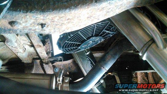 Underside view of a vehicle's exhaust pipe and an electric fan mounted near the engine