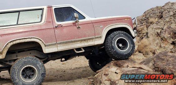 Red and white 1981 Ford Bronco climbing rocks, side view