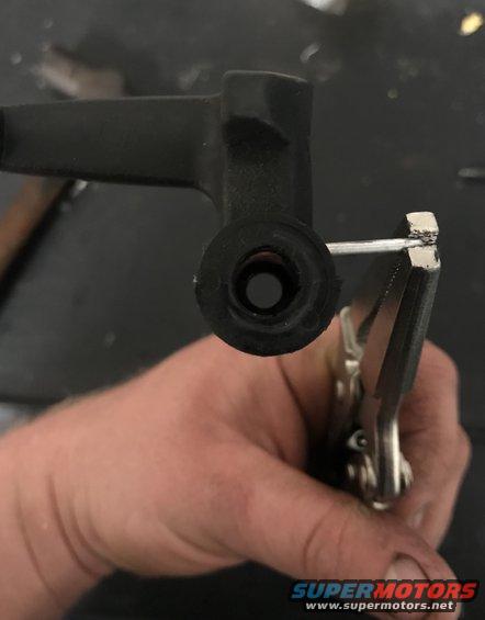Hand using pliers to hold a black automotive part with a metal pin inserted