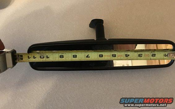 Measuring a black rear-view mirror with a tape measure. The tape shows about 10.5 inches