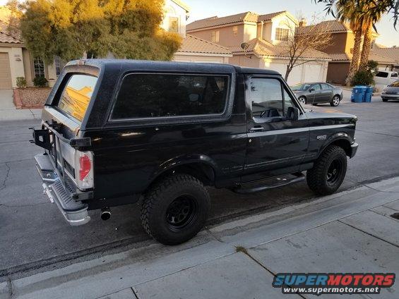 Black Ford Bronco parked on a residential street, rear-mounted spare tire, aftermarket wheels