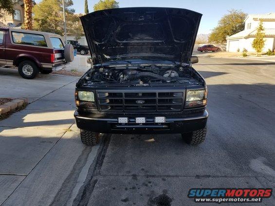 Black Ford Bronco with hood open, parked next to a maroon Ford Bronco. Engine bay visible