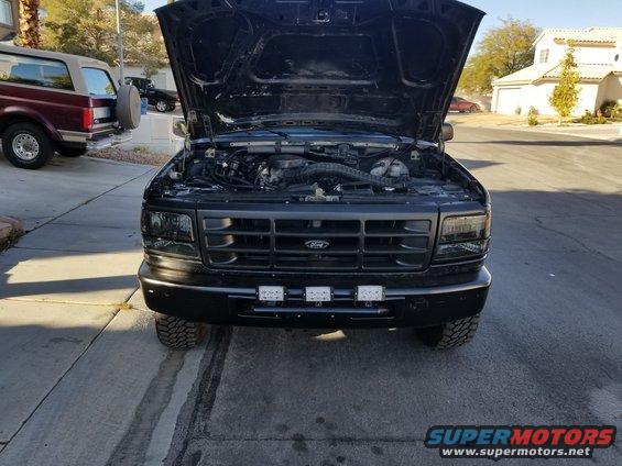 Black Ford F-Series truck with hood open, showing engine. Another maroon SUV is parked to the left
