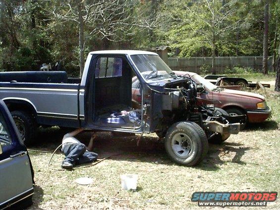 guy working under a pickup truck, another car parked behind it