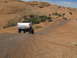 1984 Ford Bronco - Several off-road vehicles navigate a dusty, rocky terrain under a clear blue sky.