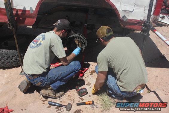 Two guys working on the rear brake assembly of a vehicle that's jacked up