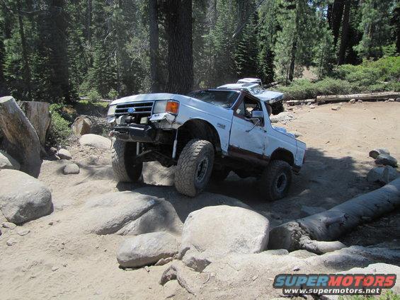 White Ford Bronco is driving over rocks with another vehicle behind it