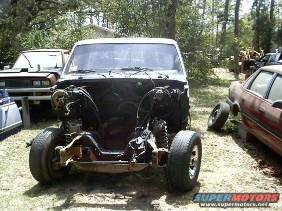 White truck chassis, front view, engine removed, tires on, parked outdoors