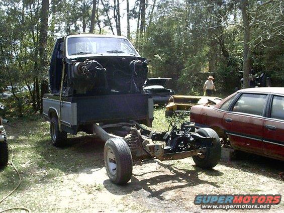 Truck chassis with cab removed, parked outdoors next to other vehicles