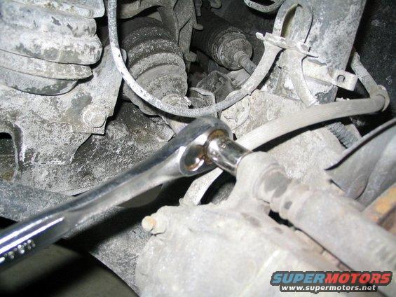 Close-up of a wrench turning a bolt on a dirty vehicle brake caliper assembly