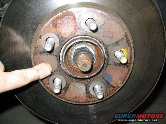 close-up of car's brake rotor and hub assembly, finger pointing to a lug nut area