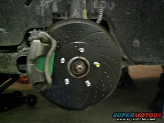 Close-up of a drilled brake rotor and green brake caliper