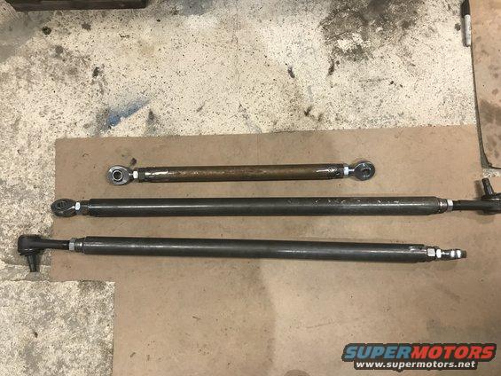 Three metal rods with threaded ends and spherical joints laid out on a cardboard surface