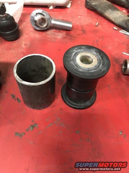 Two black rubber suspension bushings and a metal tube on a red surface
