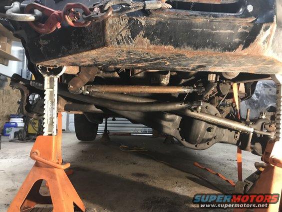 Vehicle underbody showing suspension and drivetrain parts, supported by jack stands