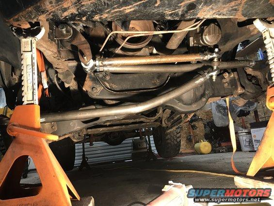 Undercarriage of a lifted vehicle, showing steering linkage and suspension components. Orange jack stands support the frame