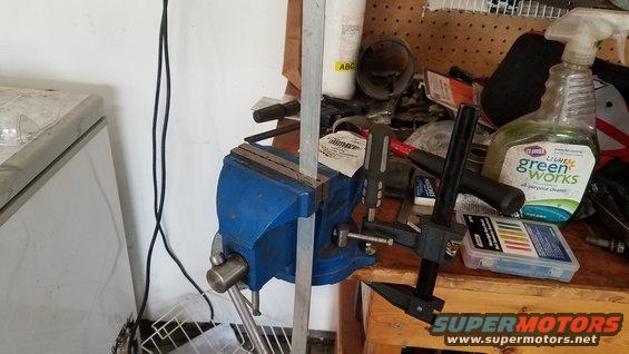 Workbench with blue vise holding metal, caliper, and cleaning spray