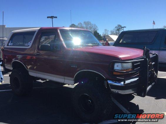 Maroon Ford Bronco with a white top and a brush guard, lifted on large tires