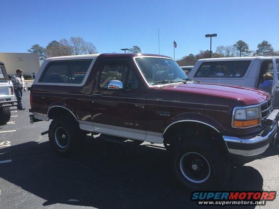 Maroon Ford Bronco SUV with white top and trim, lifted suspension. Another white SUV is parked next to it