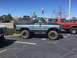 1979 Ford Bronco - A lifted blue Ford Bronco is parked next to another Bronco in a parking lot on a sunny day.