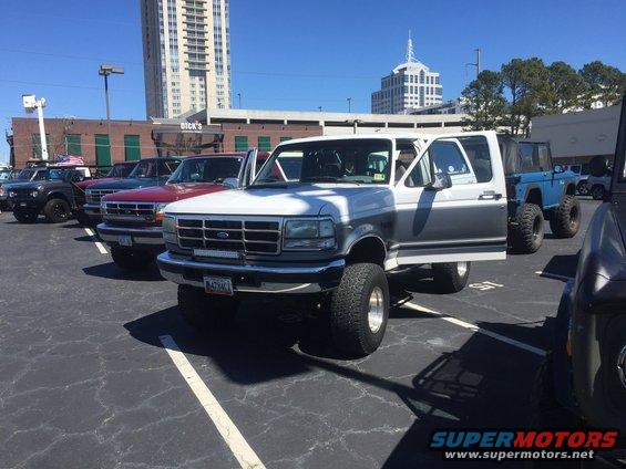 Two-tone white and grey Ford Bronco with driver's door open, lifted suspension, and aftermarket light bar