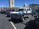 1979 Ford Bronco - A line of lifted trucks and SUVs are parked in a lot, with a white and grey Ford Bronco in the foreground.