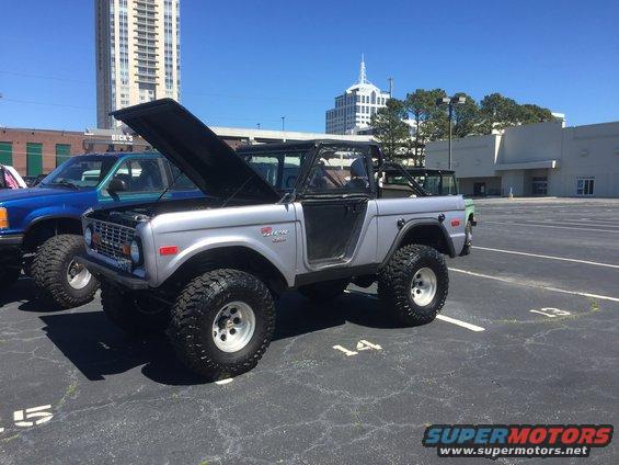 Silver Ford Bronco with hood open, parked next to a blue truck