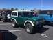 1979 Ford Bronco - A green 1979 Ford Bronco with a white hardtop is parked in a lot, alongside other SUVs.