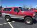 1979 Ford Bronco - A red and silver Ford Bronco is parked in a lot with other vehicles under a clear blue sky.