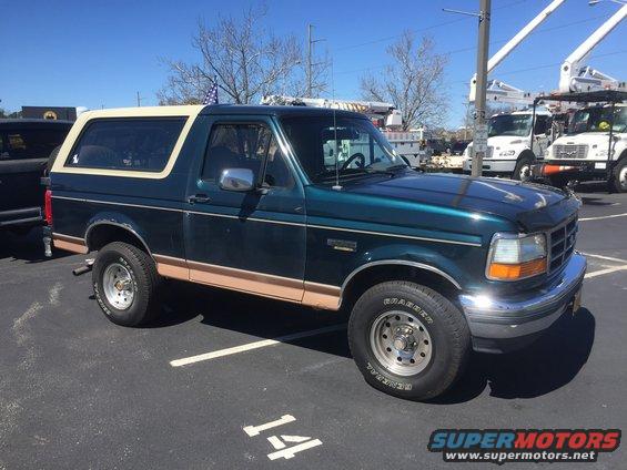 Green Ford Bronco with tan trim and a white top parked in a lot