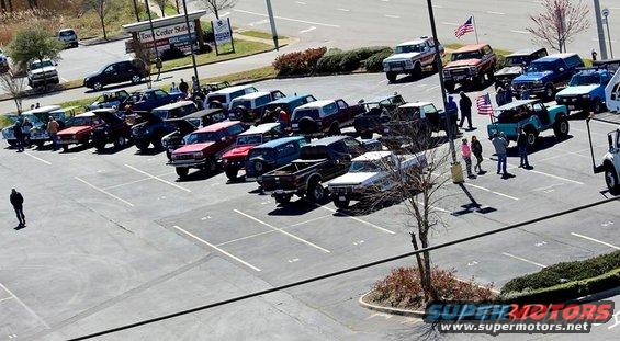 1979 Ford Bronco and other trucks parked in lot, some with American flags