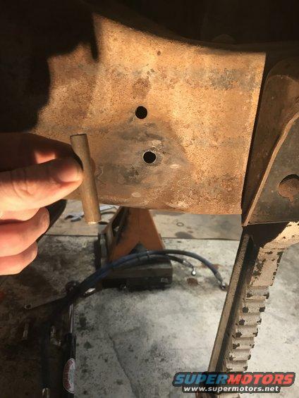 Rusty frame section with holes and a hand holding a metal rod