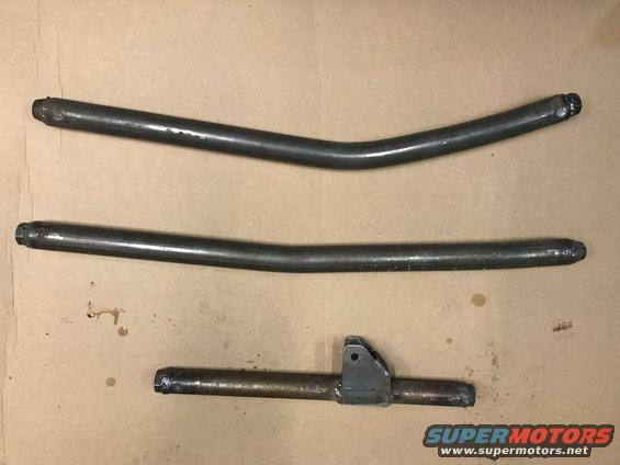 Three metal pipes, two curved and one straight with a bracket, laid out on a brown surface. Supermotors.net logo visible