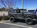 1979 Ford Bronco - A dirty black Ford Bronco is parked in a lot next to another Bronco.