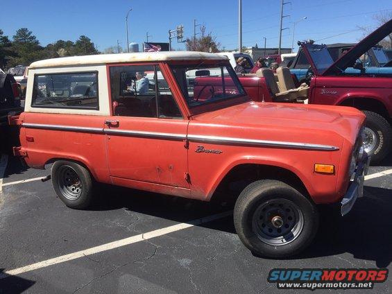 Orange Ford Bronco with a white hardtop, seen from the side