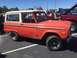 1979 Ford Bronco - An orange Ford Bronco with a white hardtop is parked in a lot next to other vehicles.
